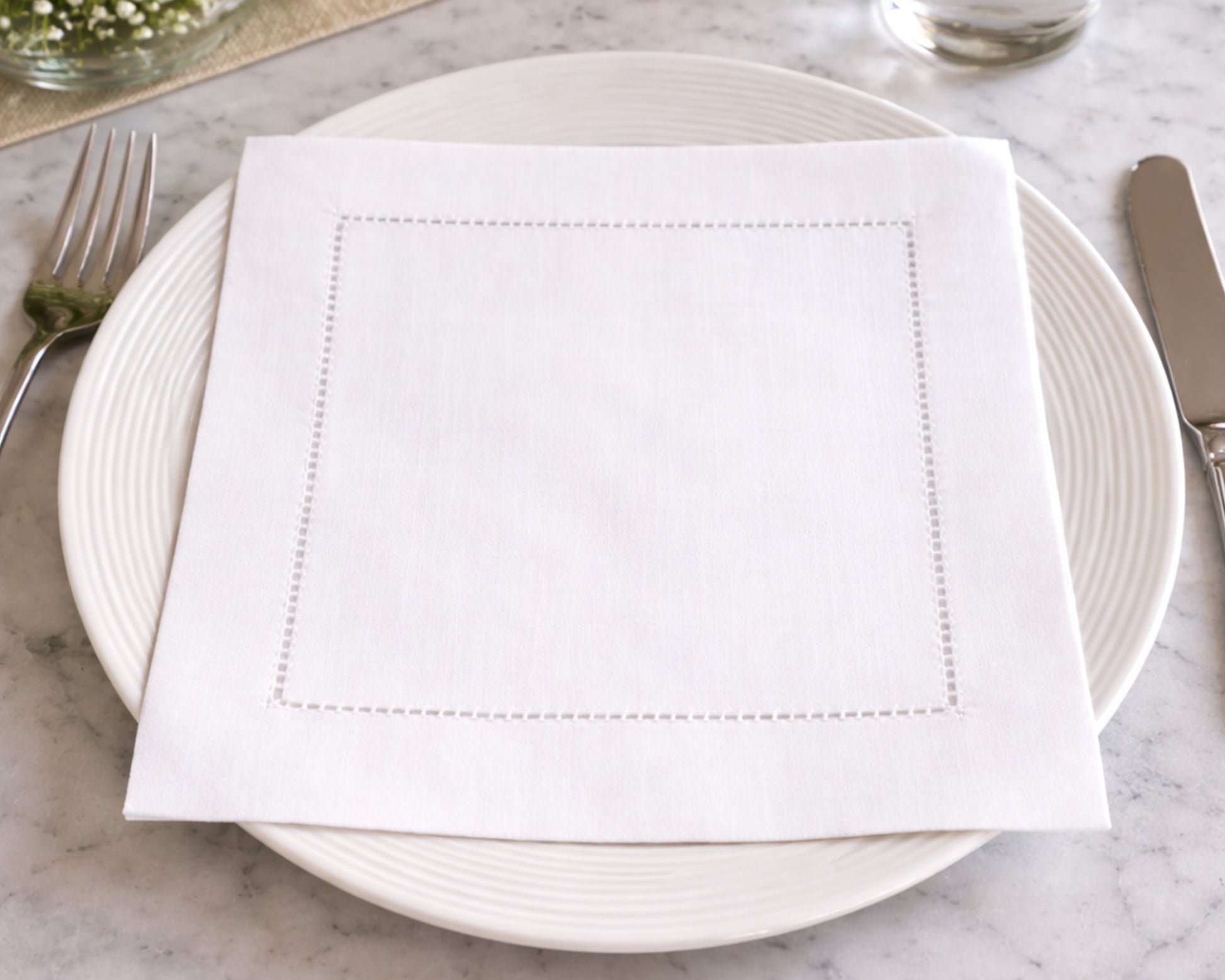 White napkin on a white plate with silverware on a marble surface