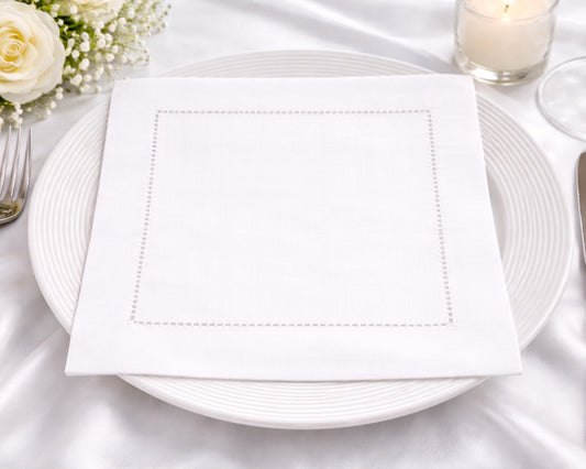 White plate with a folded white napkin on a white tablecloth.