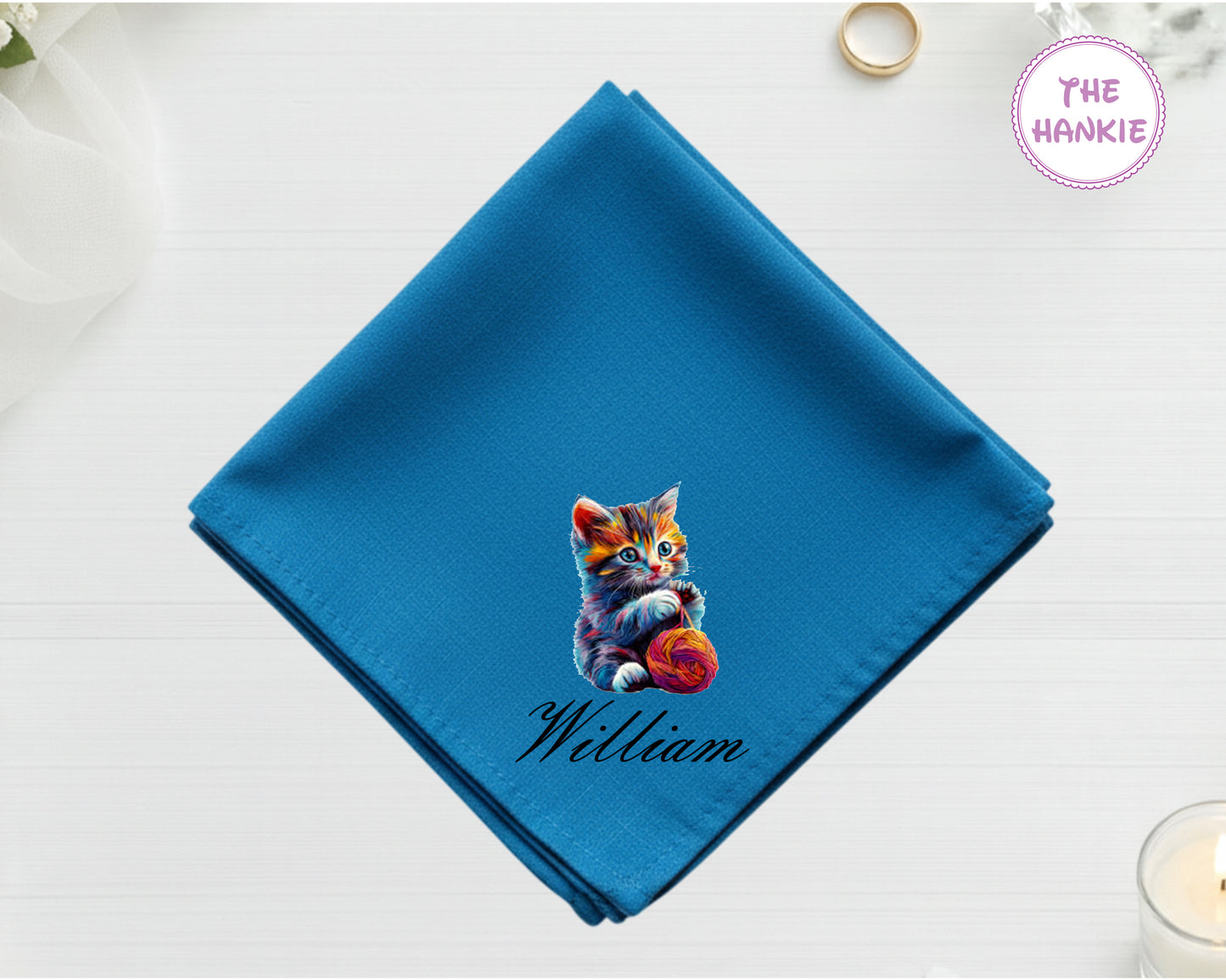 A sapphire blue cotton pocket square featuring the name "William" and a detailed digital print of a multi-colored kitten playing with a ball of yarn.