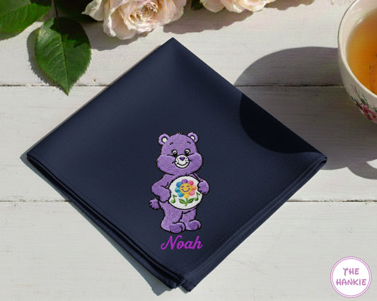 A crisp white cotton handkerchief personalized with the name "Willow" in golden script next to a vibrant, fuzzy-textured honey bee embroidery.