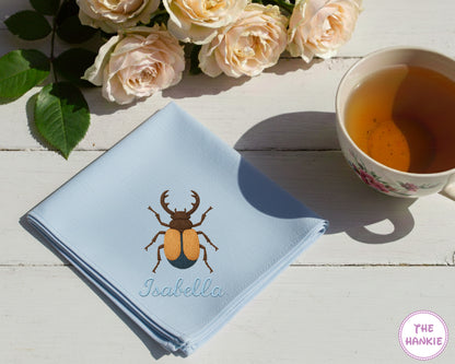 A crisp white cotton handkerchief featuring the name "Willow" and a large, vibrant orange and pink embroidered butterfly.